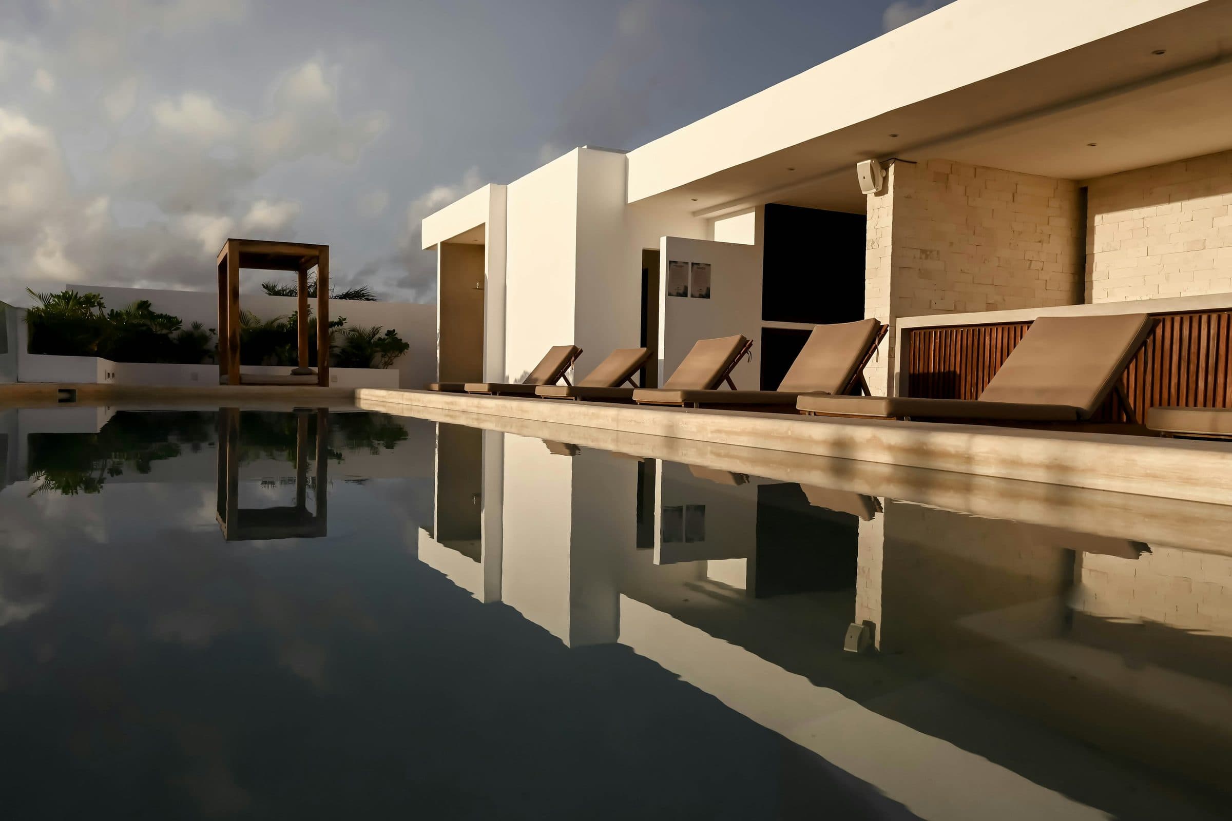 The villa across the pool in late light, the living room open on two sides behind it.