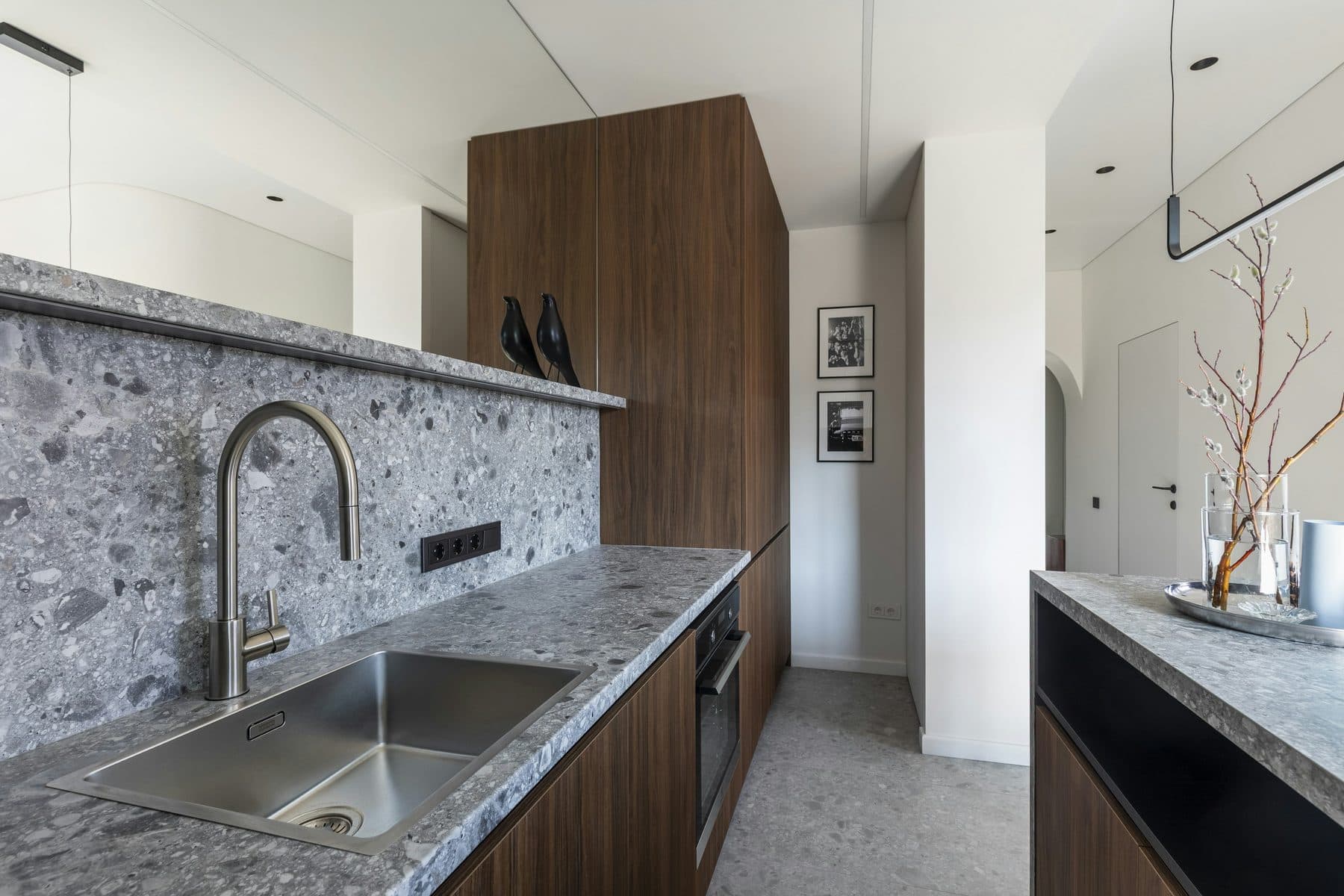 The kitchen: a long stone counter, induction hob, and open shelving in teak.