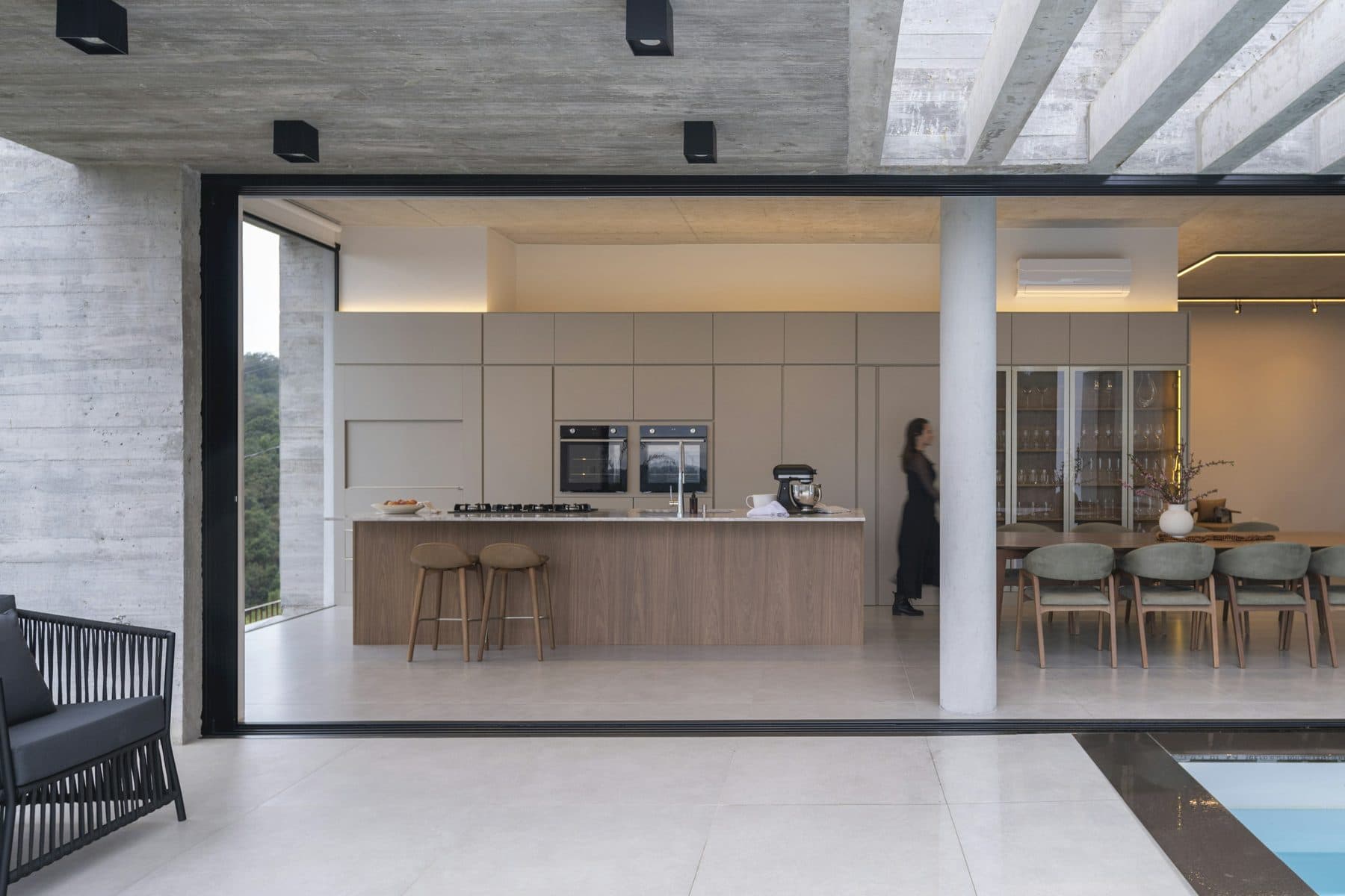 The living room open on two sides, low seating facing the terrace and the pool beyond.