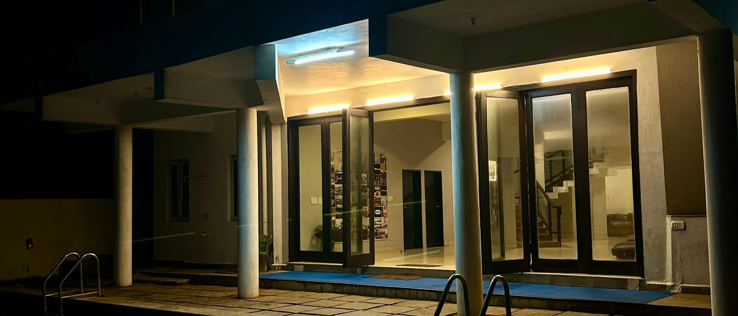 The villa at dusk, the pool lit from below and the concrete wall in shadow.