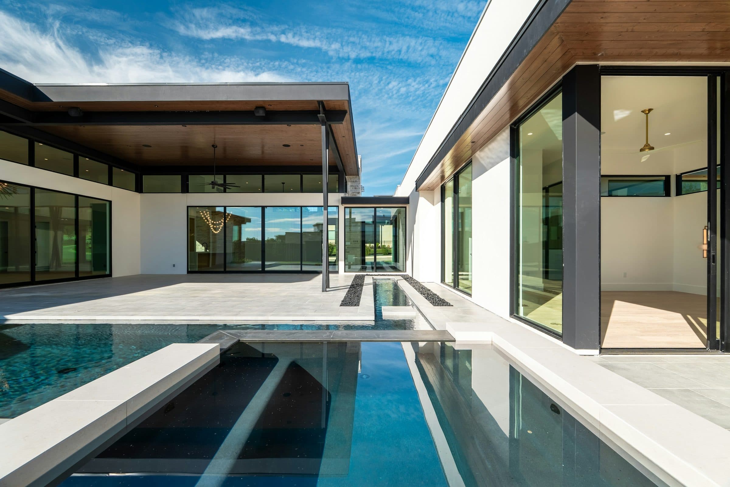 The villa at afternoon light: a board-formed concrete wall, full-height glass, and the pool in the foreground.