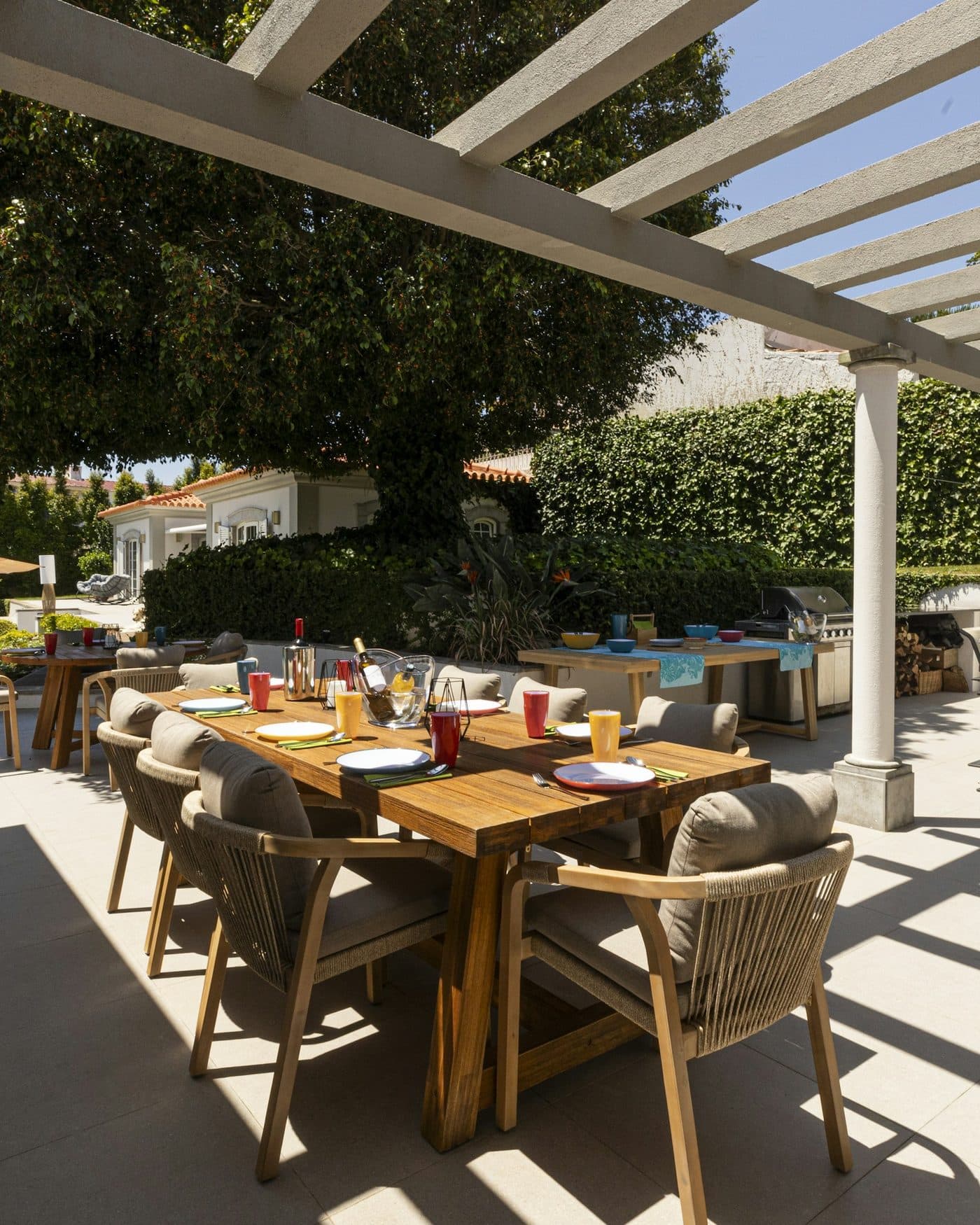 The covered terrace running the length of the pool, a dining table for six in the shade.
